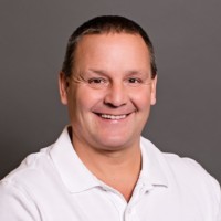 Bill Thoennes is smiling warmly while wearing a white polo shirt against a gray background.