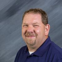 A man wearing a navy blue polo shirt, embroidered with